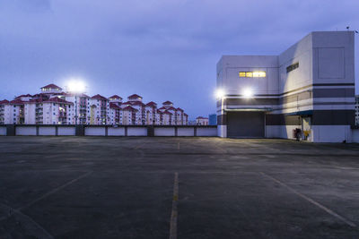 Illuminated street amidst buildings against sky at night