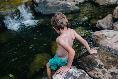 Rear view of shirtless boy on rock