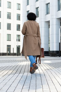 Rear view of woman walking on footpath against building