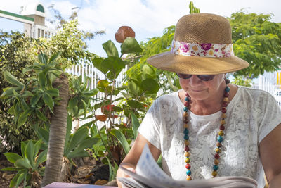 Woman wearing hat and sitting against plants