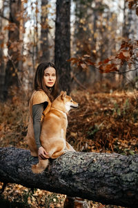 Full length of young woman sitting on tree trunk