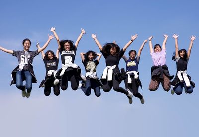 Portrait of friends jumping against clear blue sky