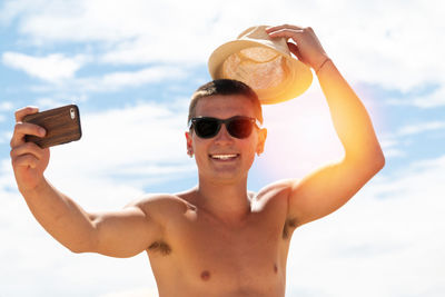 Portrait of young man using mobile phone against sky