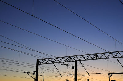 Low angle view of silhouette power lines against clear sky during sunset