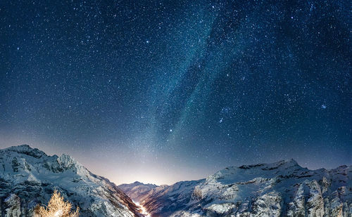 Scenic view of snowcapped mountains against stars at night