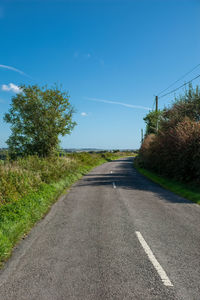 Empty road amidst trees on field against blue sky