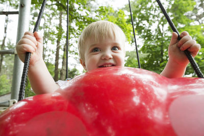 Cute baby boy swinging on red plastic swing at playground