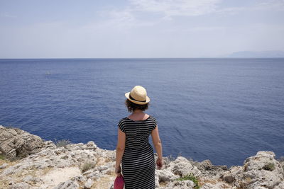 Rear view of woman standing on cliff against sea