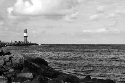 Lighthouse on beach against cloudy sky