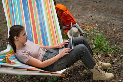 Caucasian woman working on laptop while sitting in a hammock in the forest. 