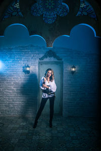 Portrait of woman in costume standing against door of abandoned building at night