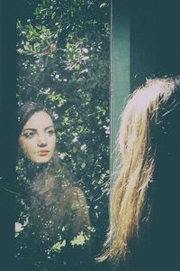 Reflection of young woman looking through window