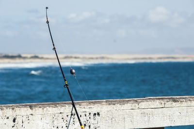 Fishing rod on pier by sea against sky