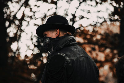 Portrait of man wearing hat standing against trees during winter