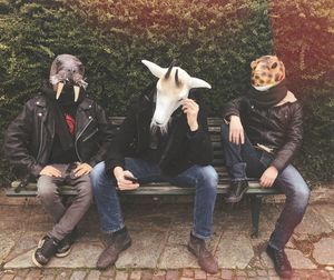 Friends wearing animal masks while sitting on bench at park