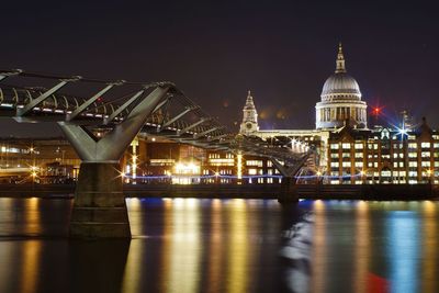 Illuminated city by river against sky at night