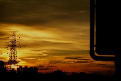 Silhouette electricity pylon against dramatic sky during sunset