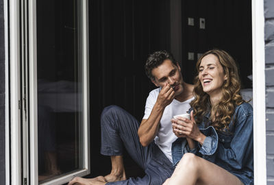 Happy couple in nightwear at home sitting at french window