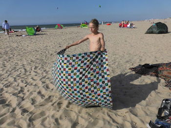 Shirtless boy holding blanket while standing at beach