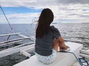 Rear view of woman sitting on boat in sea against sky