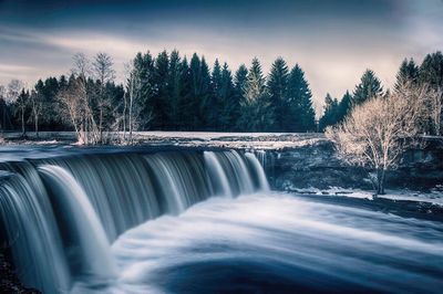 Scenic view of waterfall in forest against sky