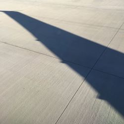 Shadow of aircraft wing on runway during sunny day