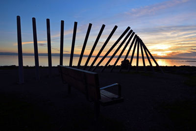 Silhouette wooden posts on beach against sky during sunset