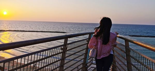 Rear view of woman looking at sea against sky during sunset