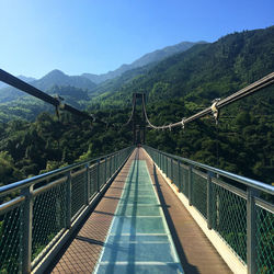 Footbridge over river in forest against clear sky