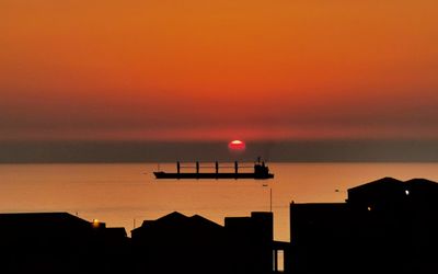 Silhouette buildings by sea against romantic sky at sunset