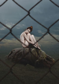 Young man sitting on chainlink fence