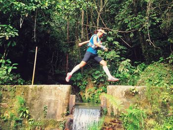 Low angle view of young woman jumping over waterfall in forest