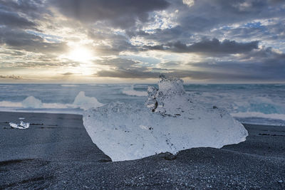 Close-up of iceberg on beautiful black sand beach against dramatic sky at sunset