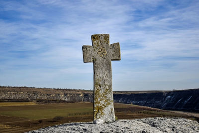 Ancient stone christian cross, mounted on cliff, near rock monastery against blue sky.