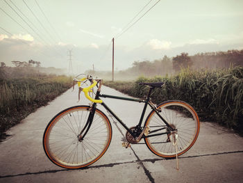 Bicycle on road amidst field against sky