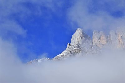 Low angle view of snowcapped mountain against fog blue sky