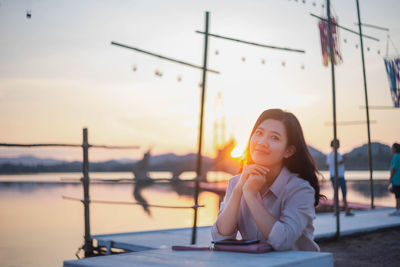 Portrait of young woman looking away against sky during sunset