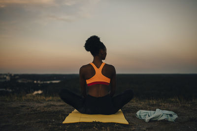 Rear view of sportswoman sitting on exercise mat during sunset