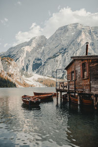 Stilt house with boats moored in lake against snowcapped mountains