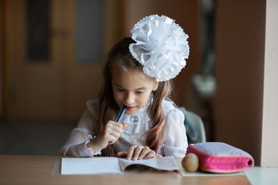 Cute girl studying while sitting by table at home