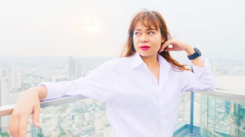 Portrait of young woman standing against sky in city