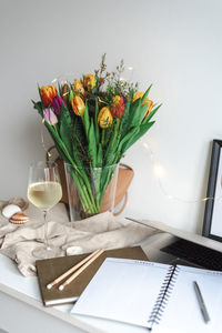 Still life with a bouquet of colorful spring tulips and a glass of white wine on the work desk.