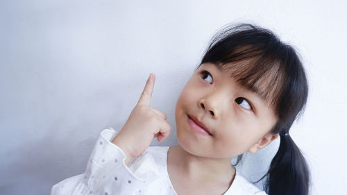 Close-up of girl pointing up against wall