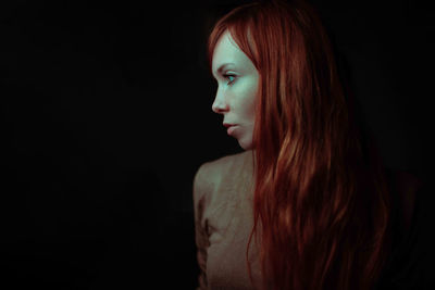 Portrait of young woman looking away against black background