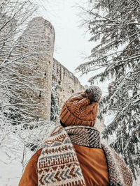 Rear view of young woman in winter clothes looking at castle ruins in winter, snow.