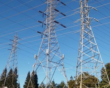 Low angle view of electricity pylon against blue sky
