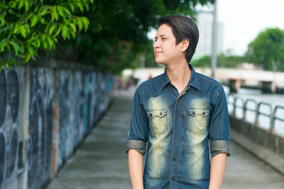 Young man looking away while standing against wall