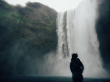 Rear view of man standing against waterfall