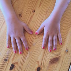 Cropped hands of woman with pink nail polish on wooden table