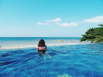 Rear view of woman standing in infinity pool against sky